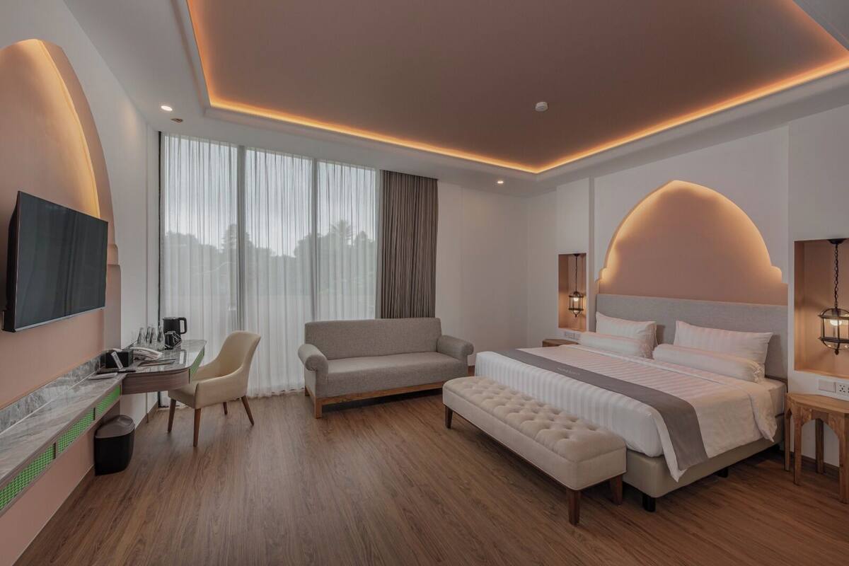 Une chambre d’hôtel moderne dotée d’un grand lit, d’un canapé, d’un bureau avec un téléviseur à écran plat et d’une grande fenêtre avec des rideaux.