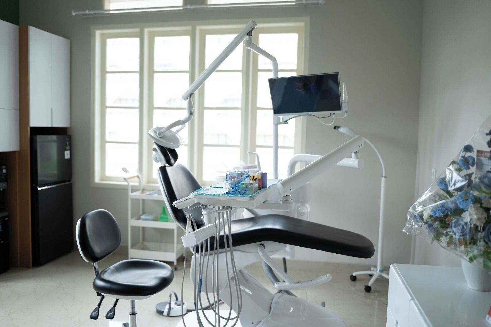 A dental clinic with a dental chair, a monitor, and a refrigerator in the background.