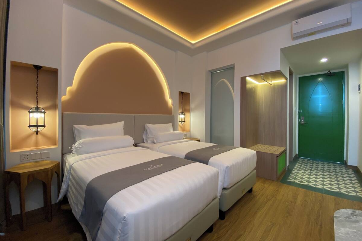 Une chambre d’hôtel avec deux lits, un plafond aux lignes courbes et une porte verte.