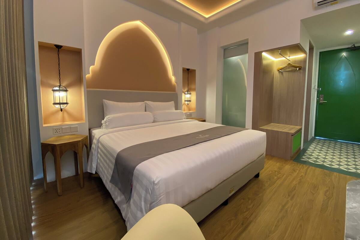 Une chambre d’hôtel moderne avec un grand lit, des lampes de chevet, une table de chevet en bois et une porte verte.