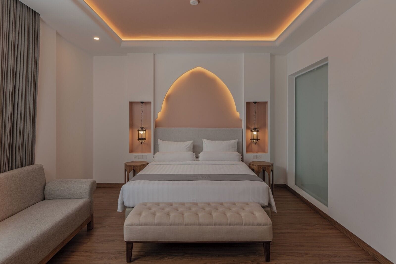 A modern bedroom with a large bed, two bedside tables, a bench, and a curved ceiling light.