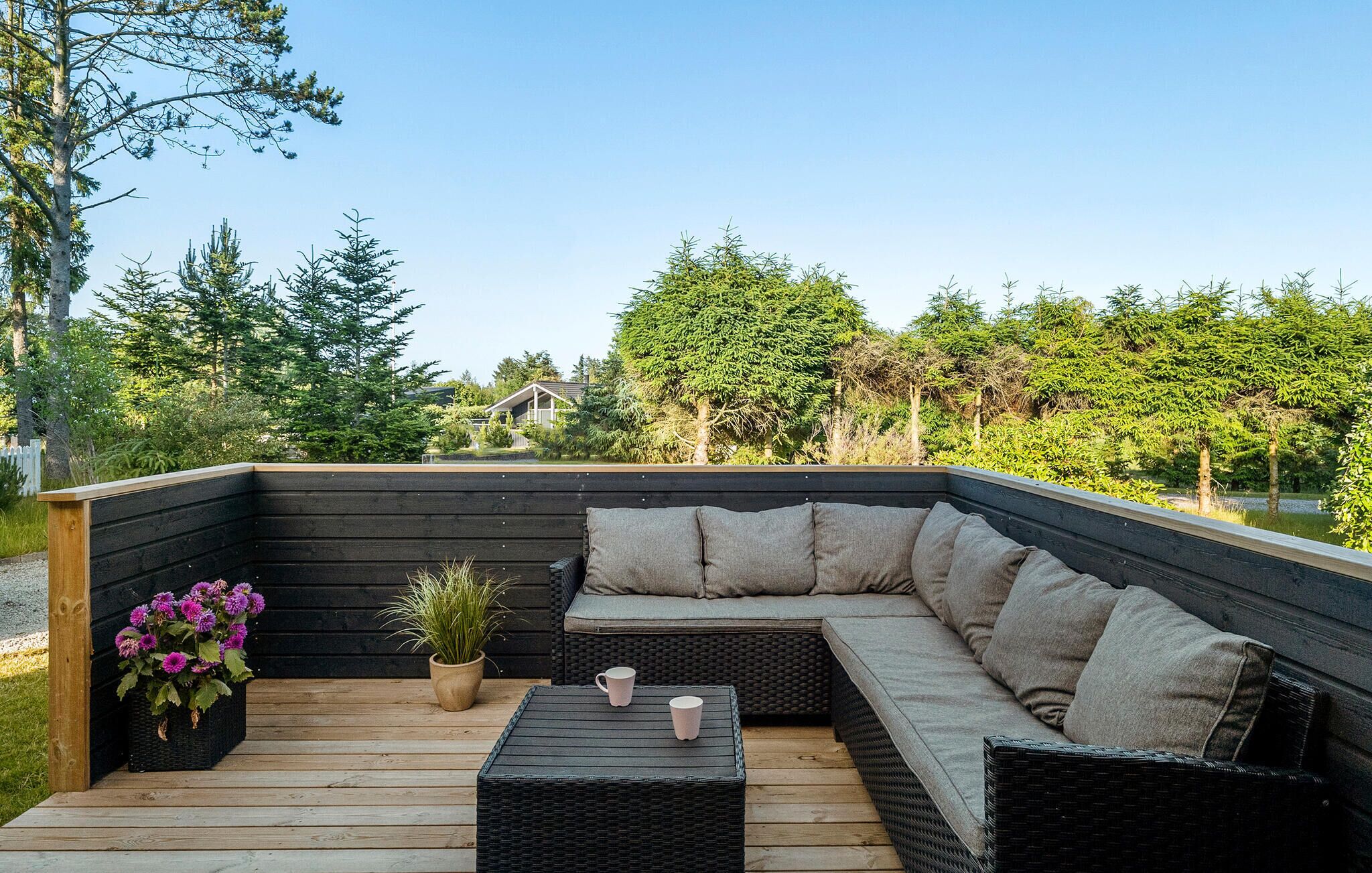 Een overdekt terras met een gebogen bank en een kleine tafel, omgeven door houten terrassen en potplanten.