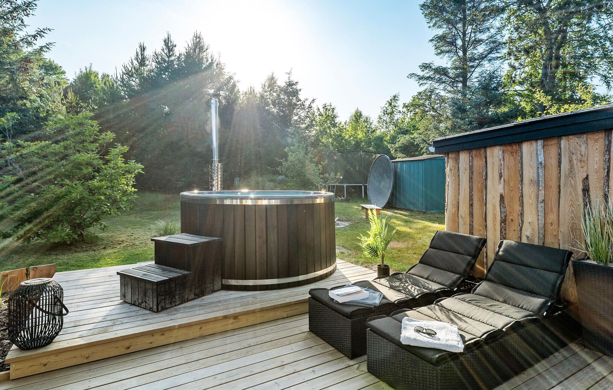 A hot tub on a wooden deck with outdoor furniture and a green fence in the background.