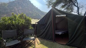 Une tente avec un lit à l’intérieur, installée sur une pelouse, avec des chaises à proximité.