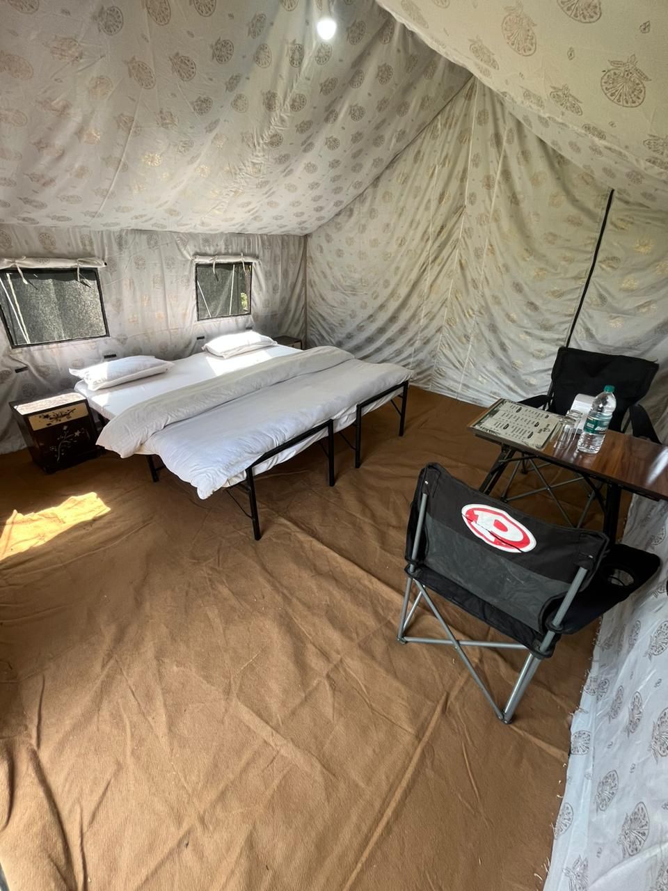 Una habitació amb tenda, un llit, una taula petita amb una cadira i una finestra.