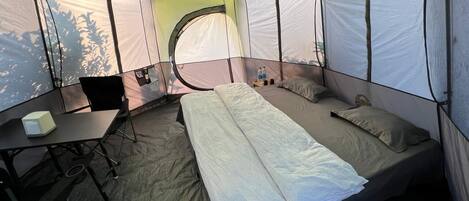 A tent with a bed, a table, and a chair.