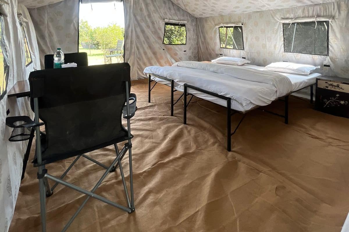 A tented room with a bed, a chair, and a table with a bottle.