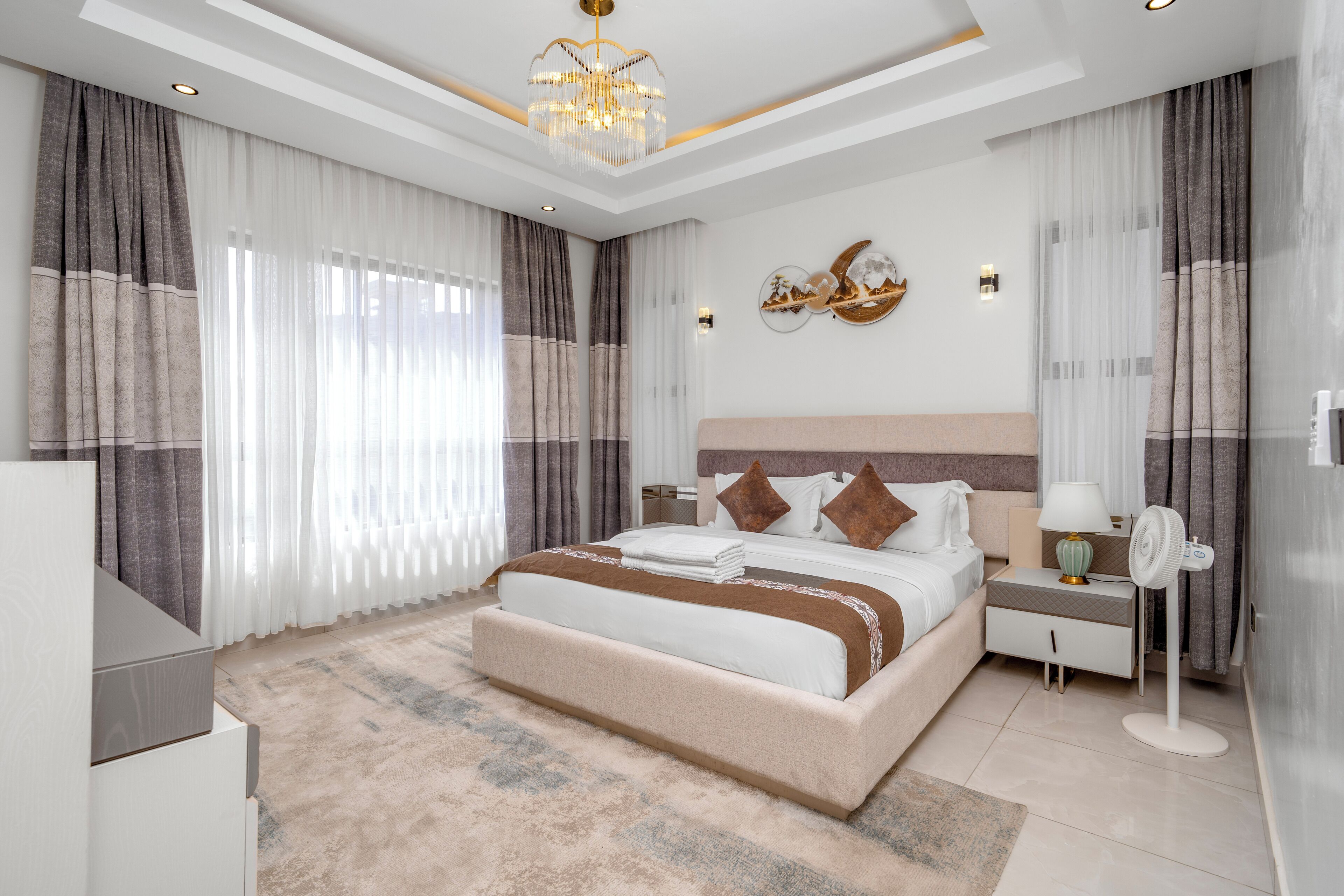 A modern bedroom with a large bed, bedside tables, a nightstand, a lamp, and a decorative wall piece.