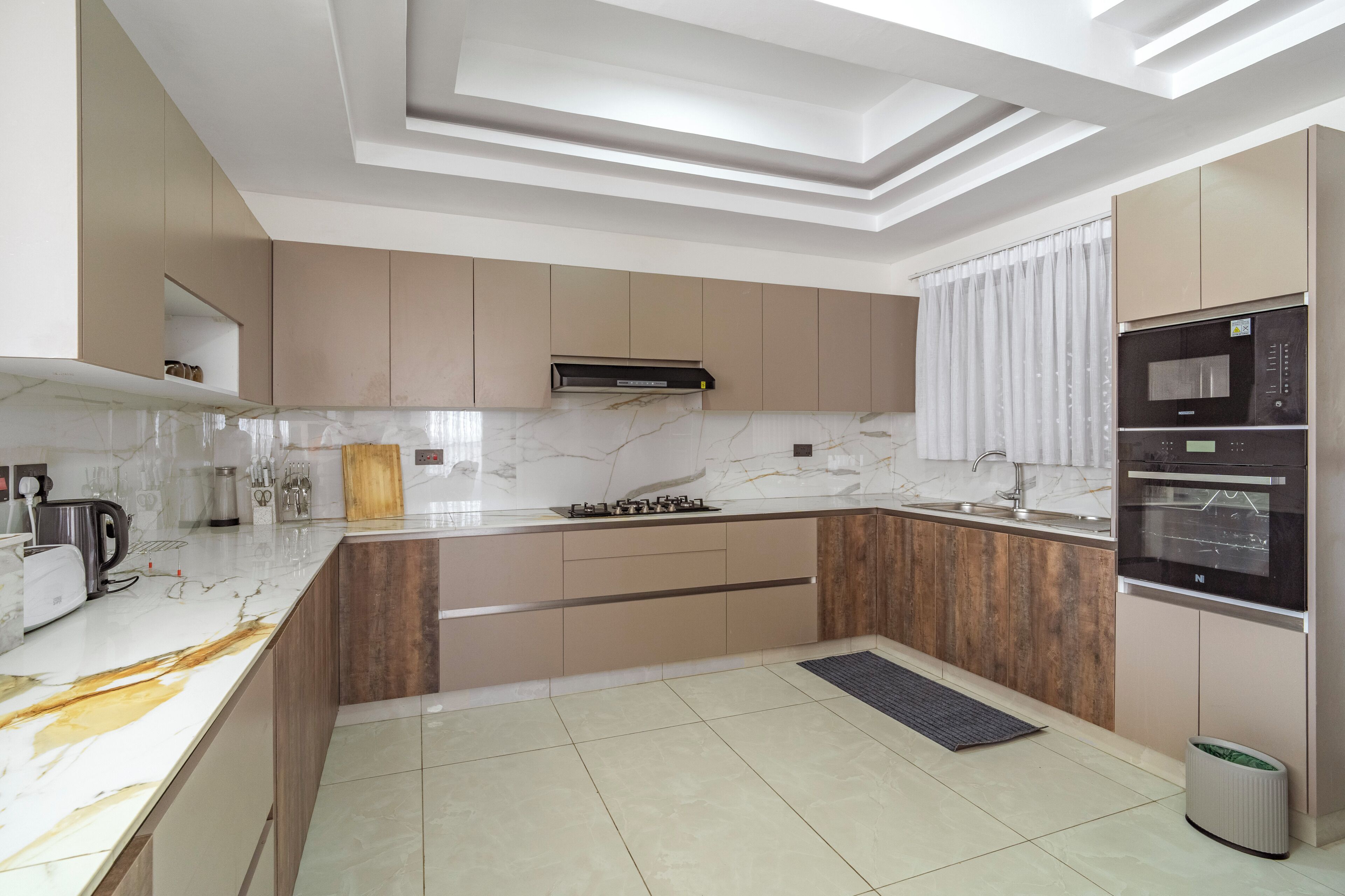 A modern kitchen with a marble countertop, built-in oven, and a wooden backsplash.