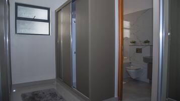 Ein Badezimmer mit Toilette, Waschbecken und Spiegel. Ein Fenster und eine Tür zu einem anderen Raum sind vorhanden.