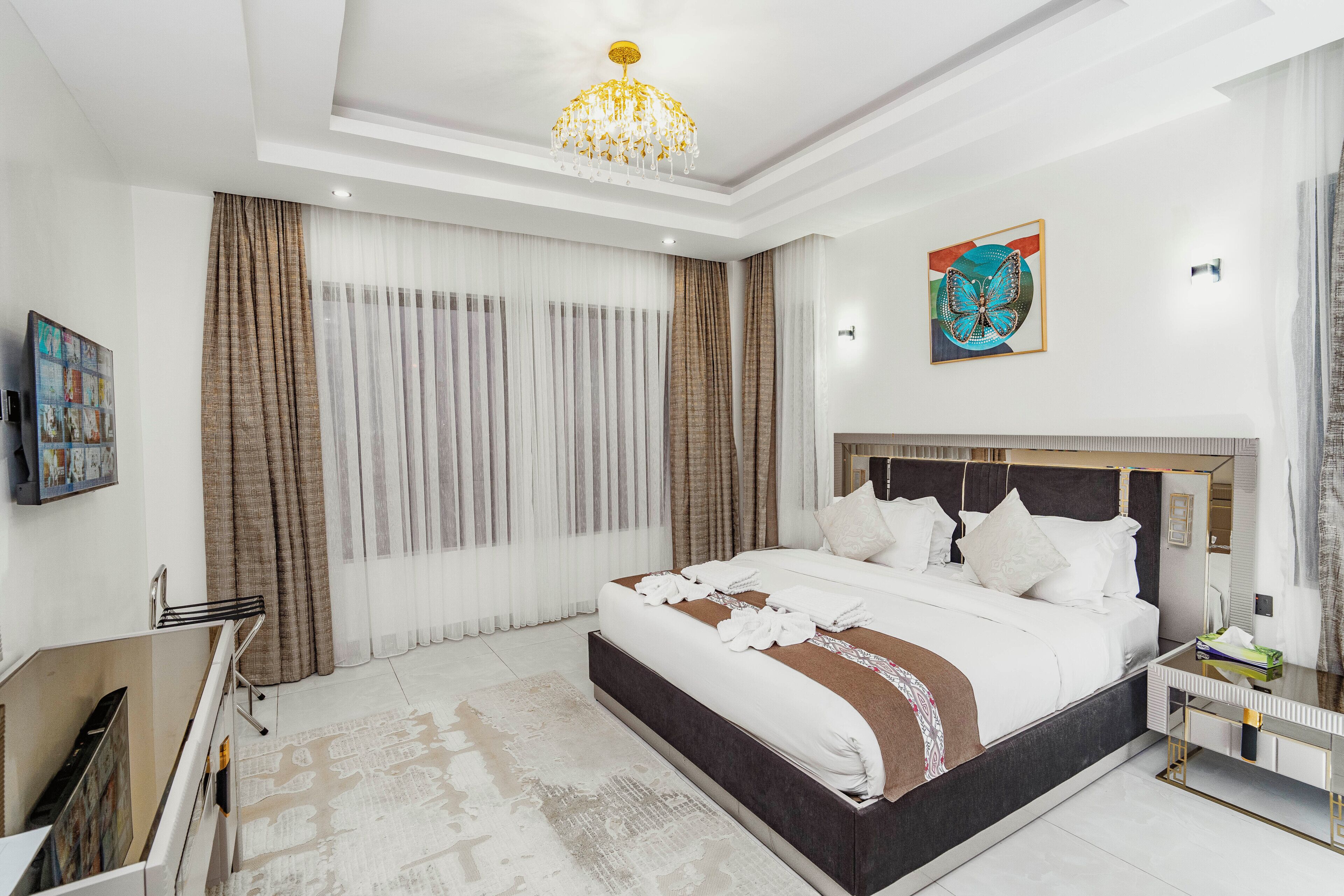 A hotel room with a large bed, a chandelier, a painting, and a view of the city.