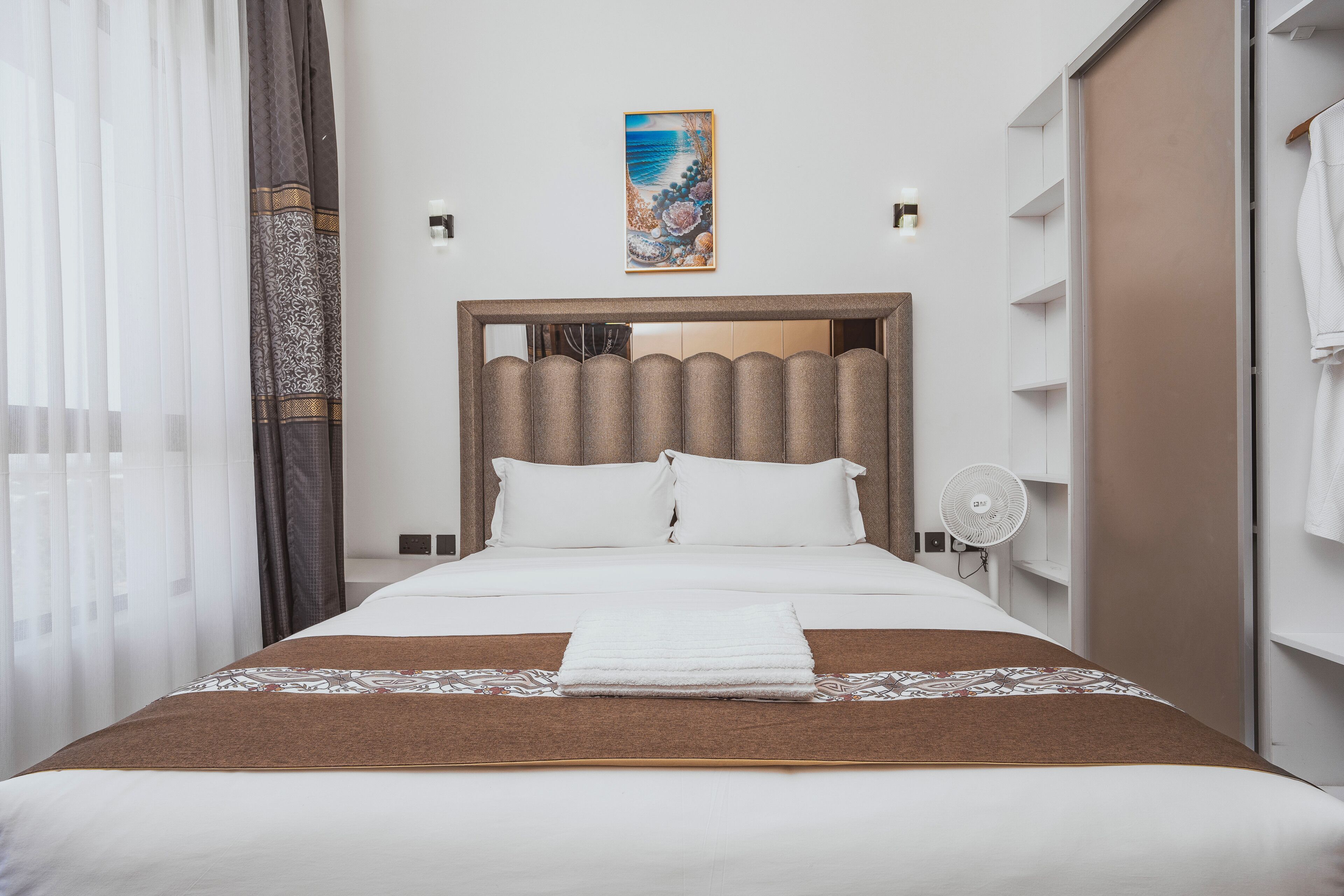 A hotel room with a large bed, a headboard, a painting on the wall, and a wardrobe.
