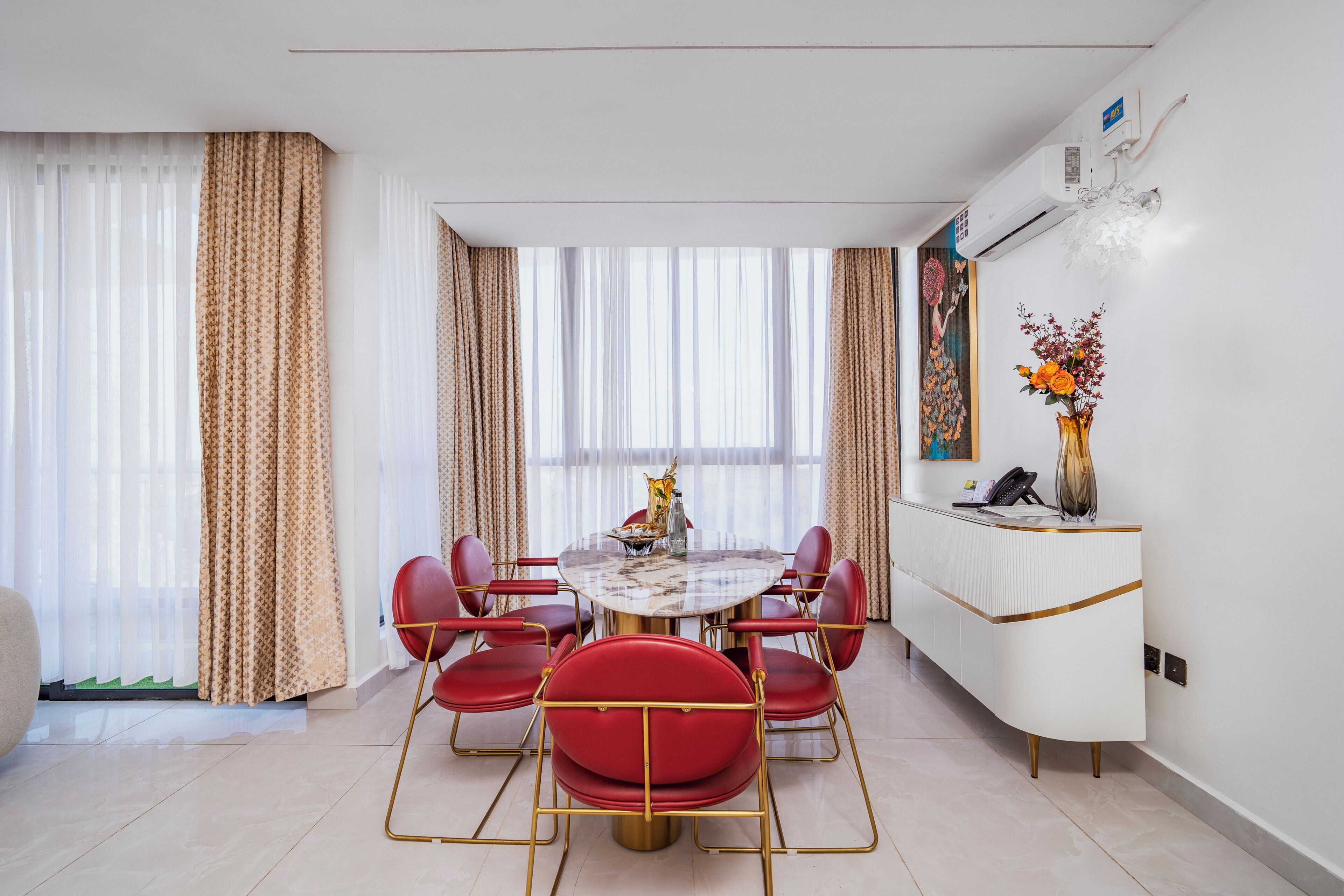 Un espace repas moderne avec une table ronde, des chaises rouges et une console blanche agrémentée d’un vase de fleurs.