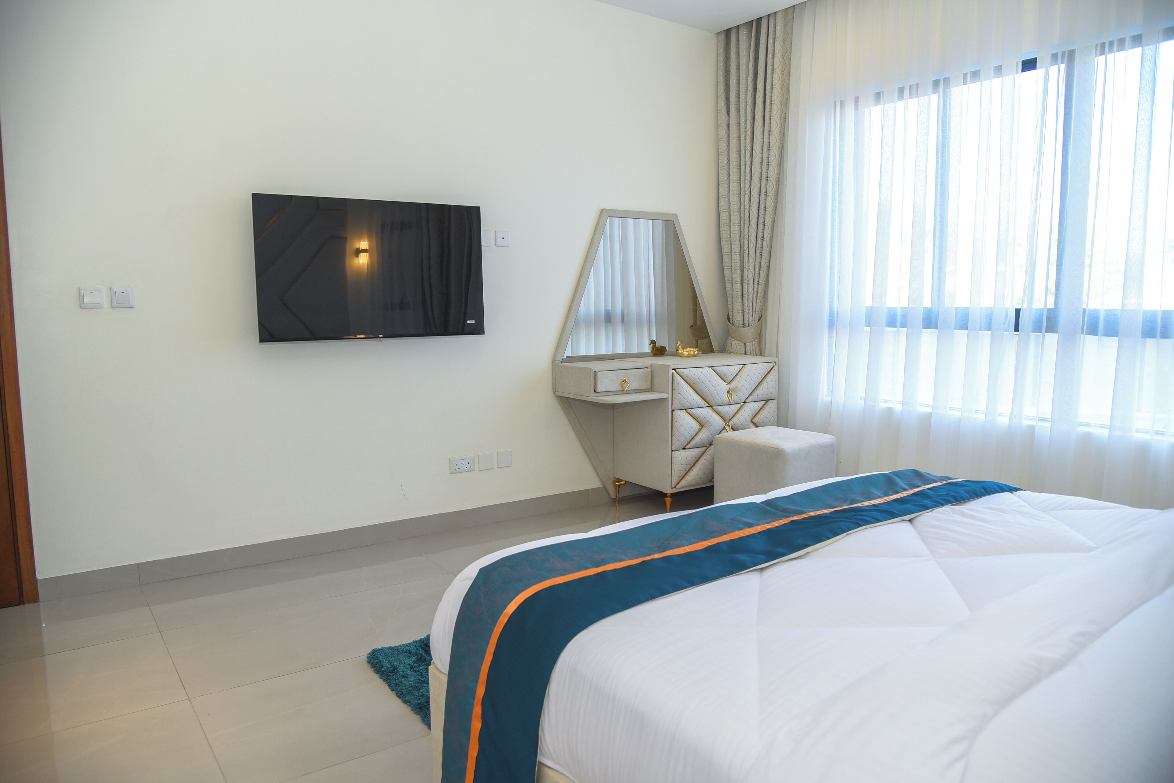 Ein Hotelzimmer mit Bett, Wand-Fernseher, Schminktisch mit Spiegel und einem Vorhangfenster.