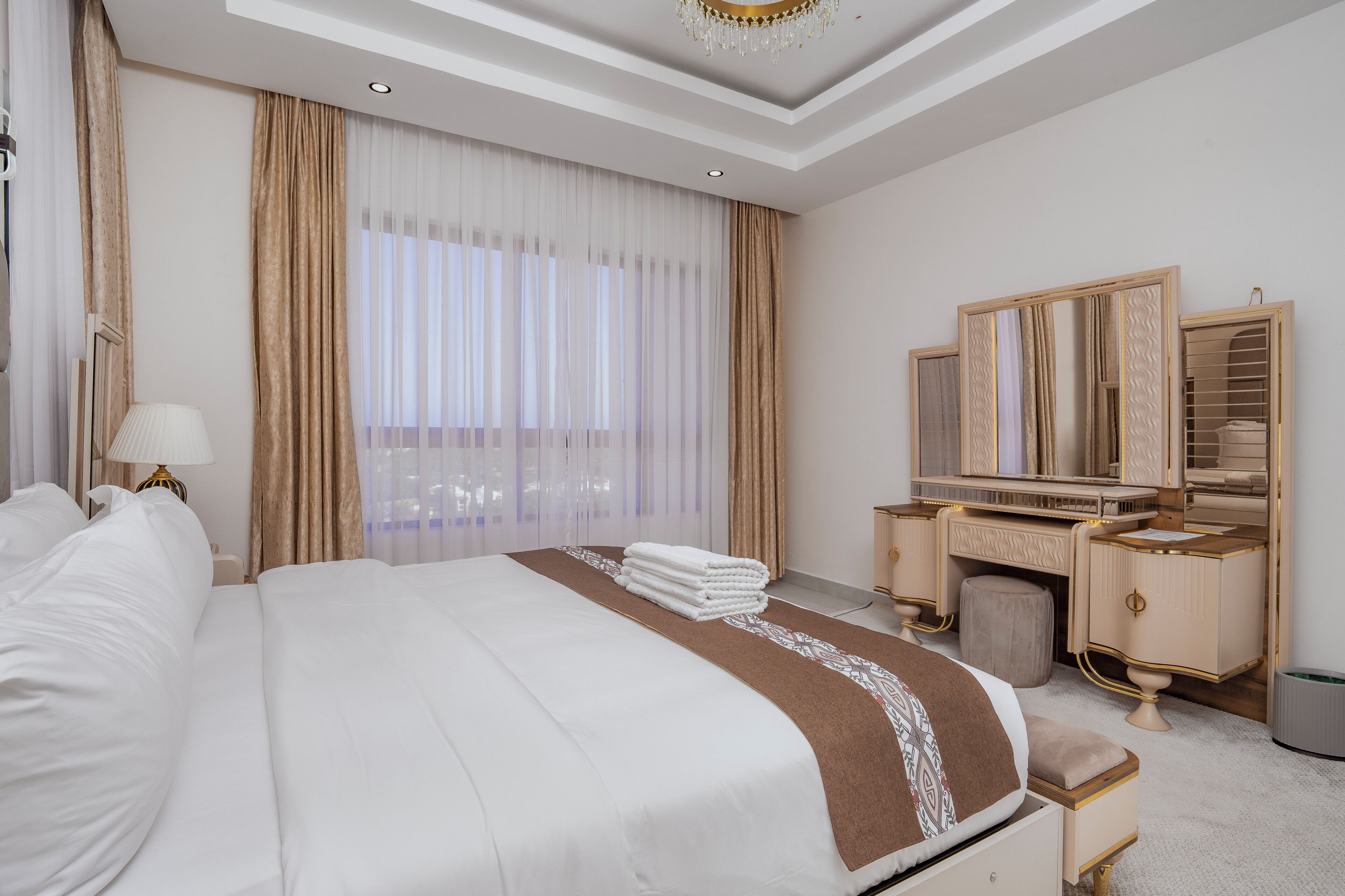 Quarto de hotel com uma cama grande, uma toucador com espelho e uma janela com cortinas.