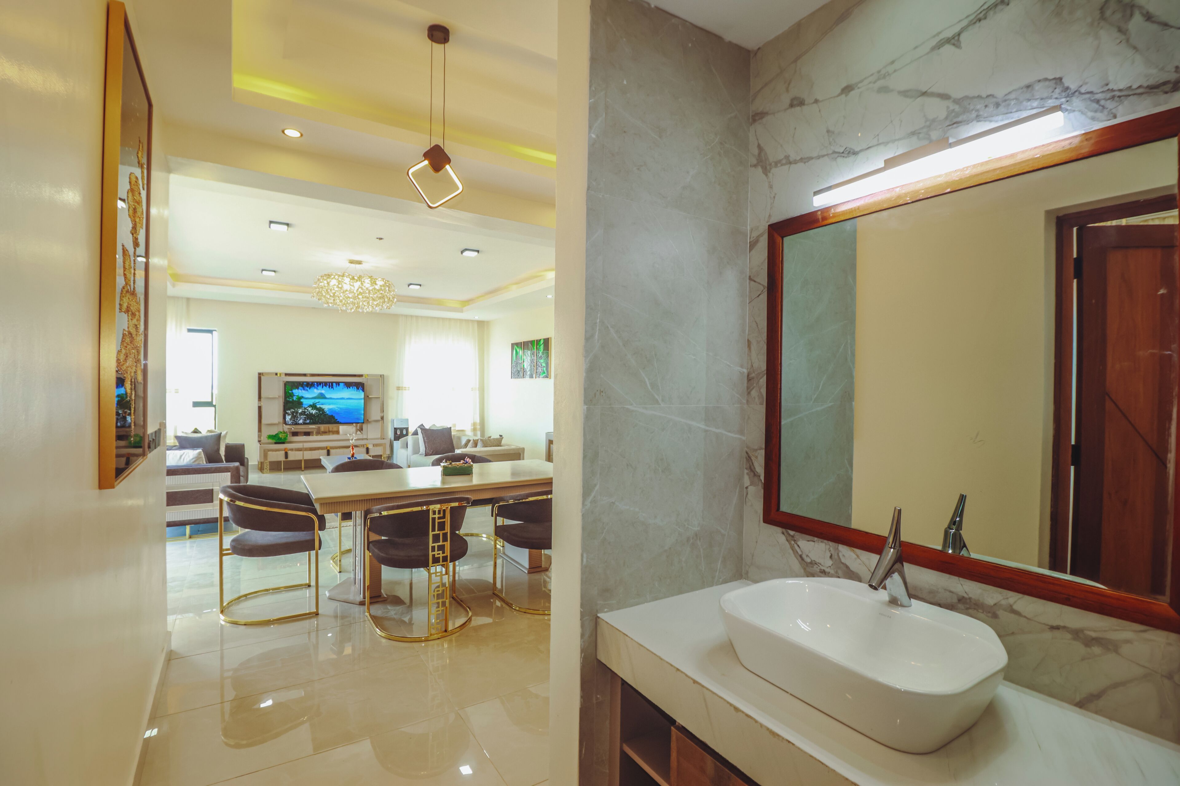 A modern interior with a dining area, a large mirror, and a bathroom with a sink and marble walls.