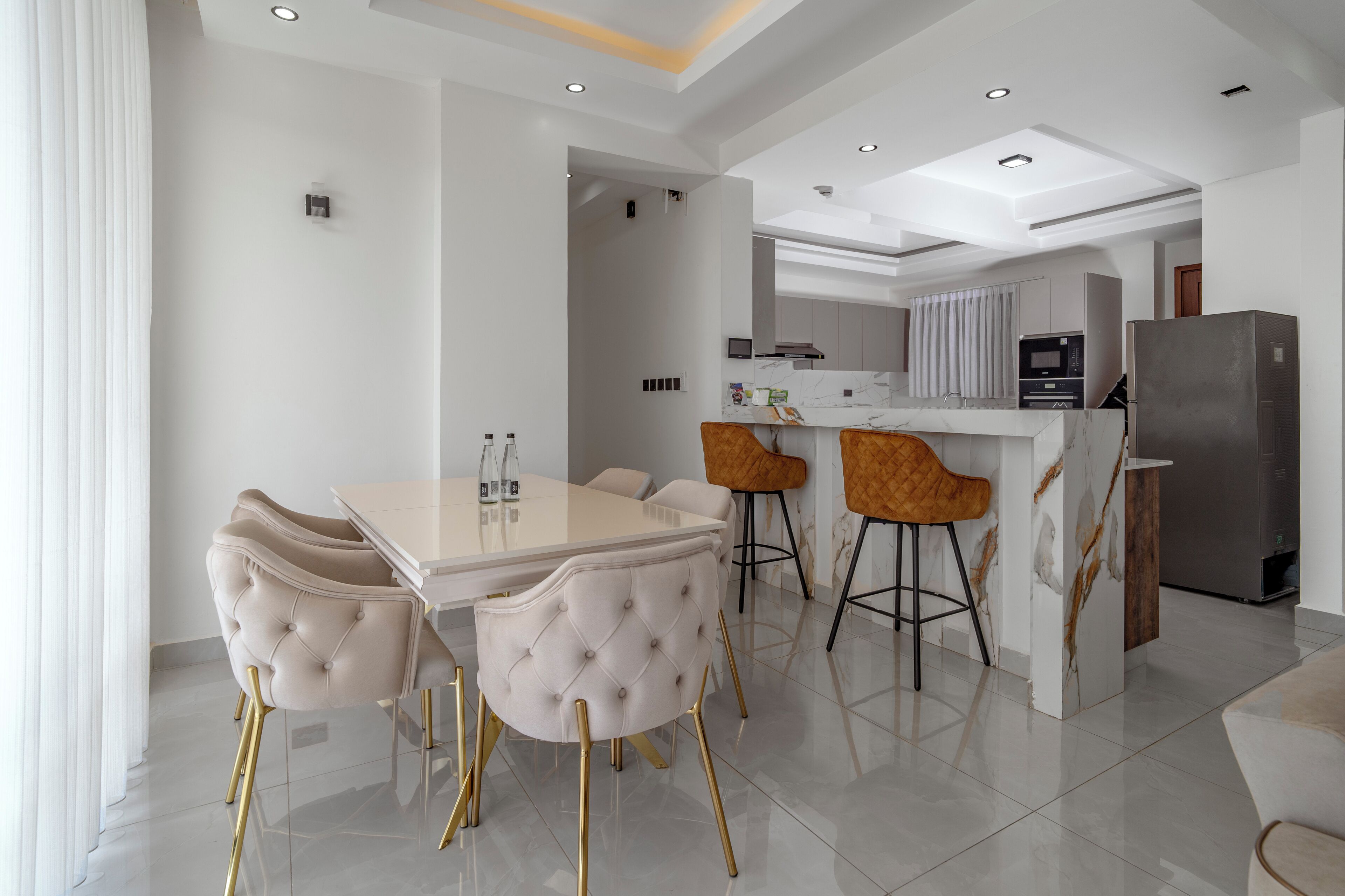 A modern kitchen with a dining area, featuring a marble countertop, a built-in oven, and a refrigerator.