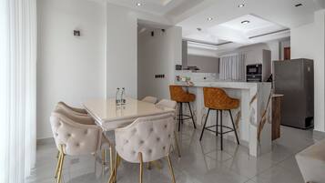 A modern kitchen with a dining area, featuring a marble countertop, a built-in oven, and a refrigerator.