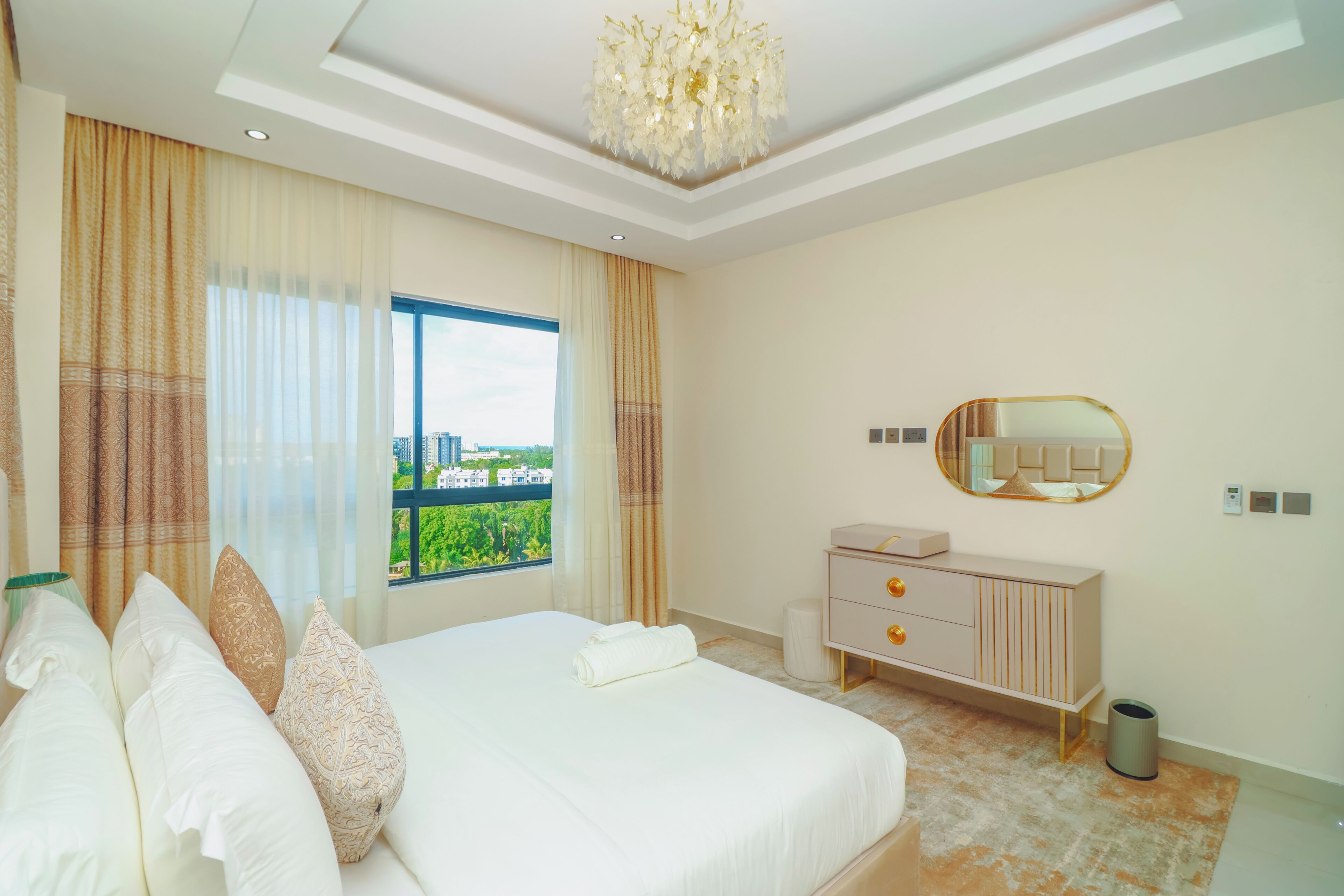 A hotel room with a large bed, a dresser, a mirror, and a view of a cityscape.