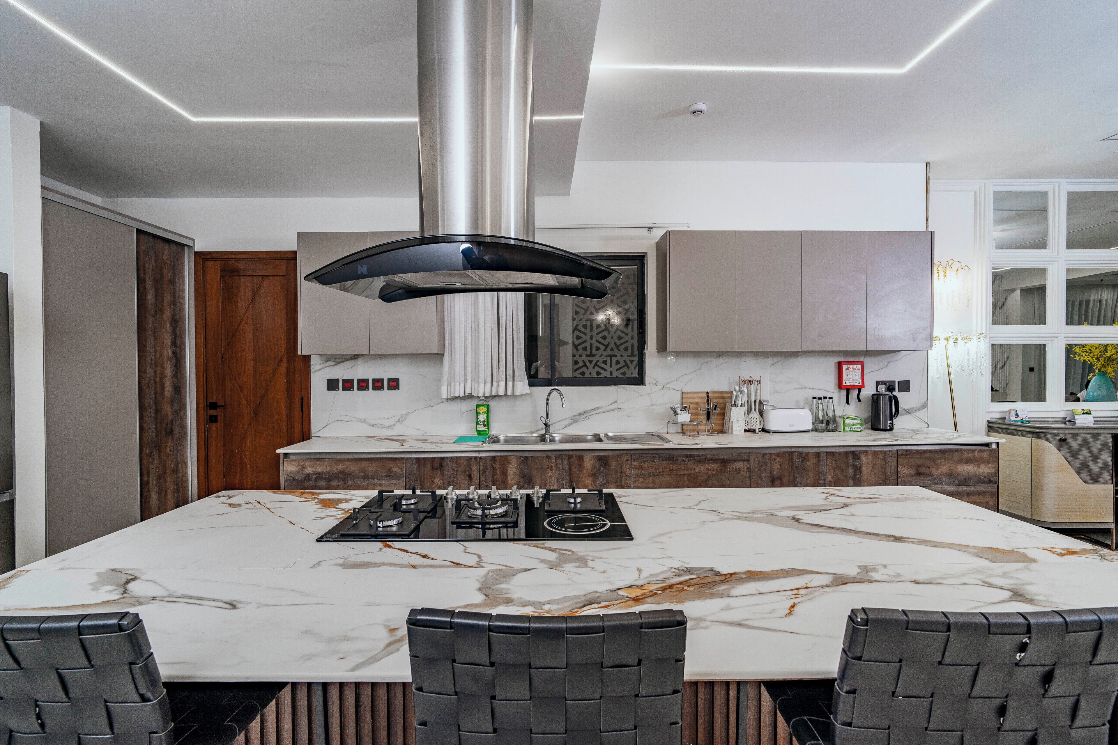 A modern kitchen with a central island, built-in cabinets, and a stainless steel range hood.