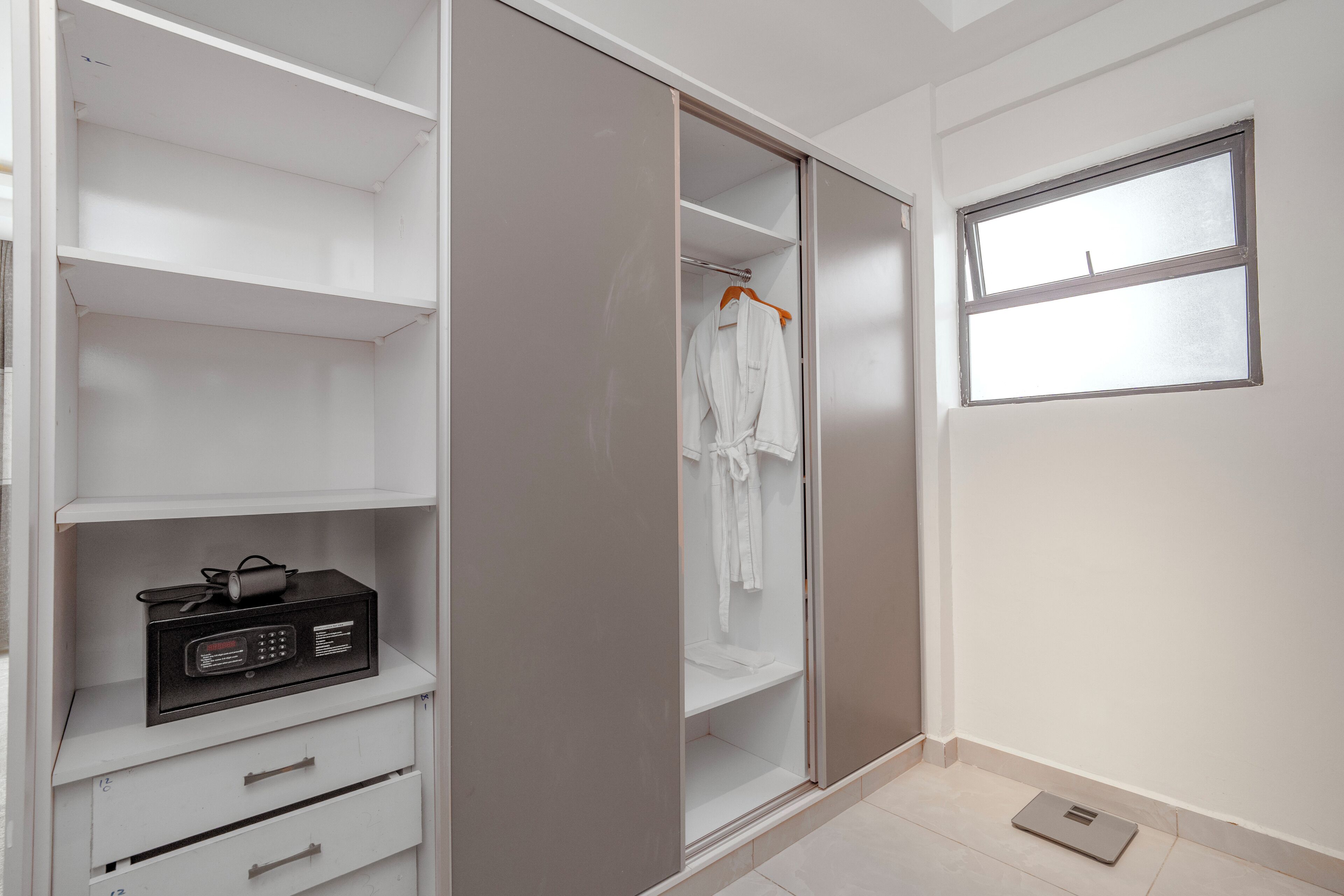 A walk-in closet with open doors, a hanging robe, and a black appliance on the left.