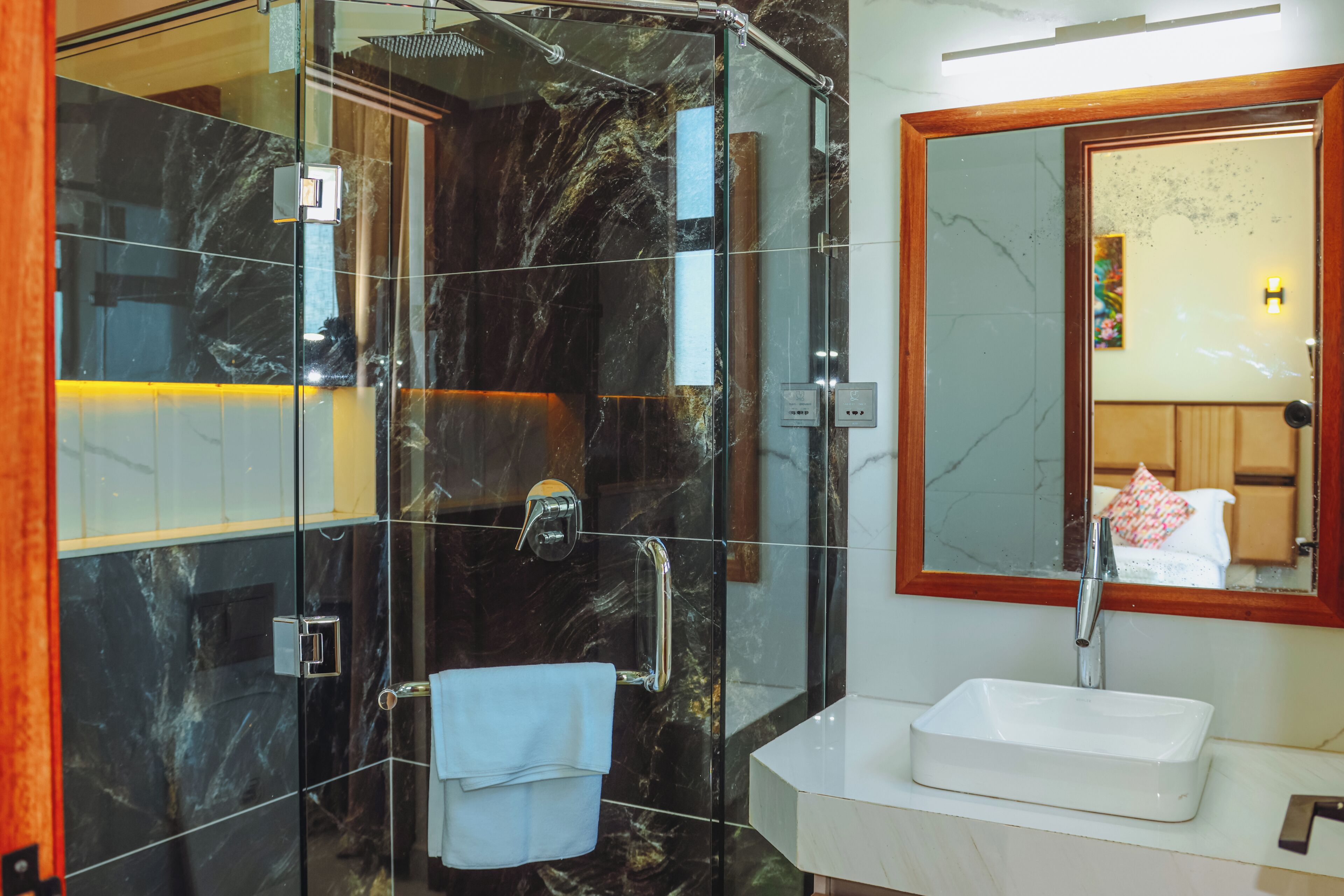 A modern bathroom with a glass-enclosed shower, a white sink, and a large mirror with a wooden frame.