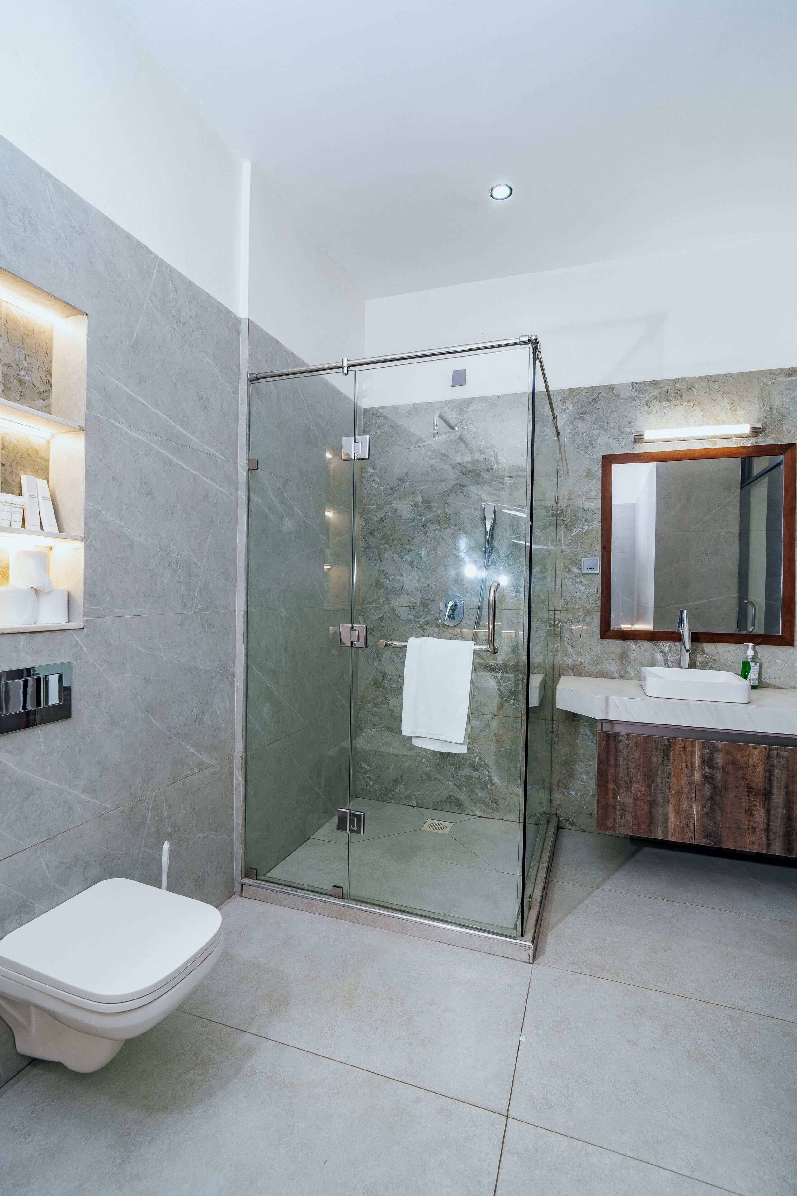 Et moderne badeværelse med en glasafskærmet brusekabine, toilet og et vaskeskab med spejl.