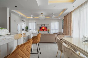 A modern living room with a marble bar, two brown chairs, a beige sofa, and a large TV screen. - Mira Heights Suite & Conferencing (Mombasa)