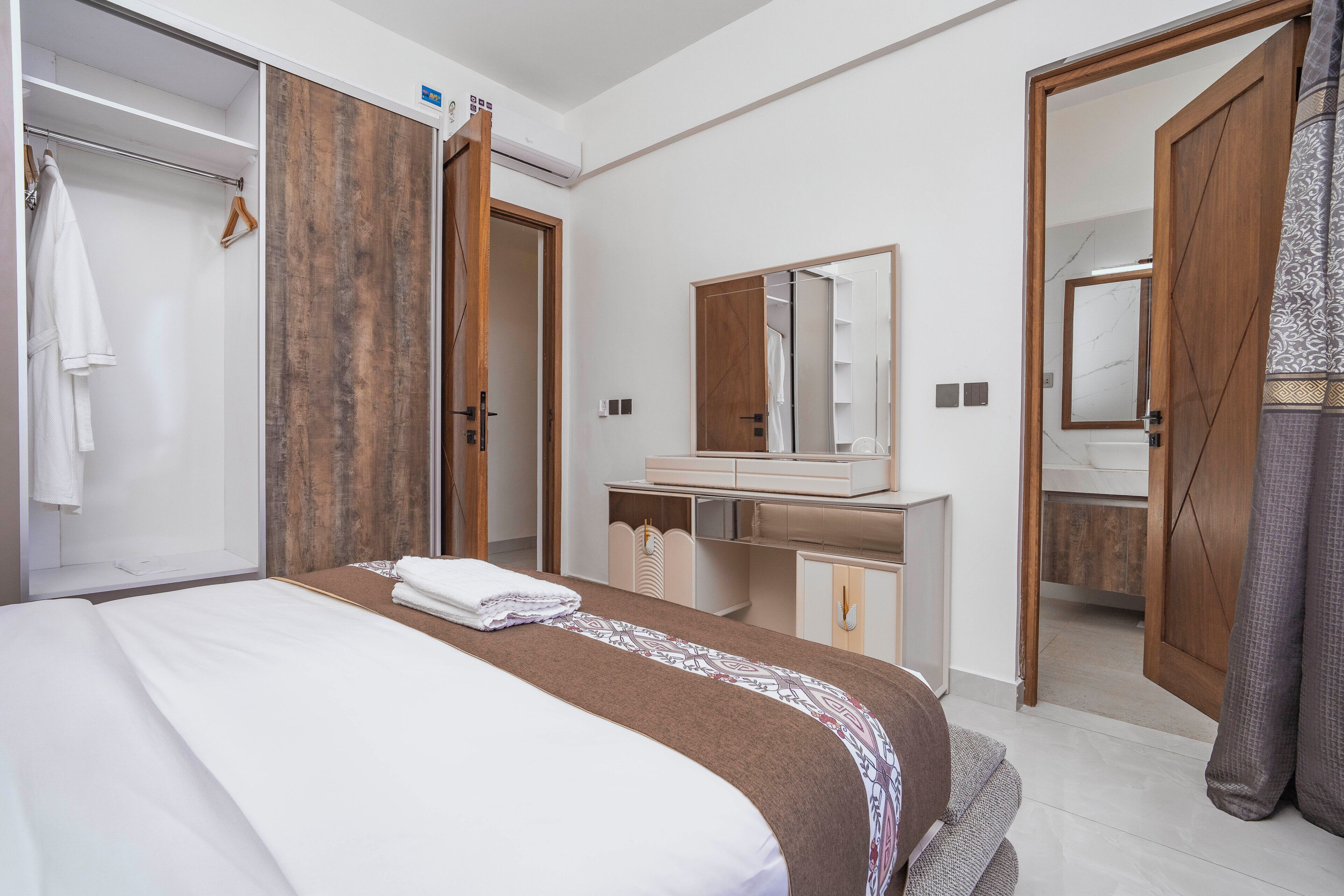 A hotel room with a bed, a bathroom with a mirror, and a wardrobe.