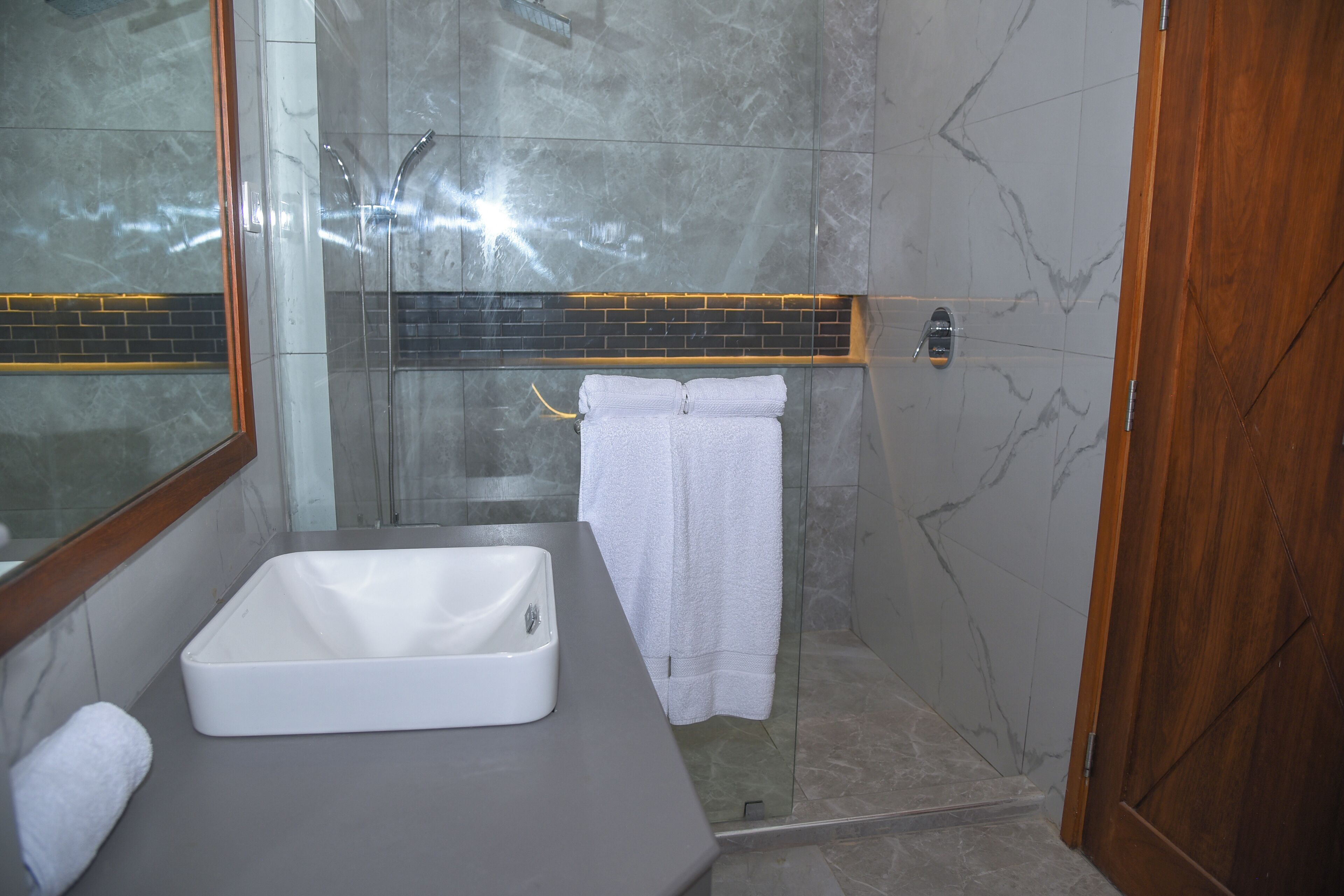 A bathroom with a white sink, a glass shower enclosure, and a wooden door.