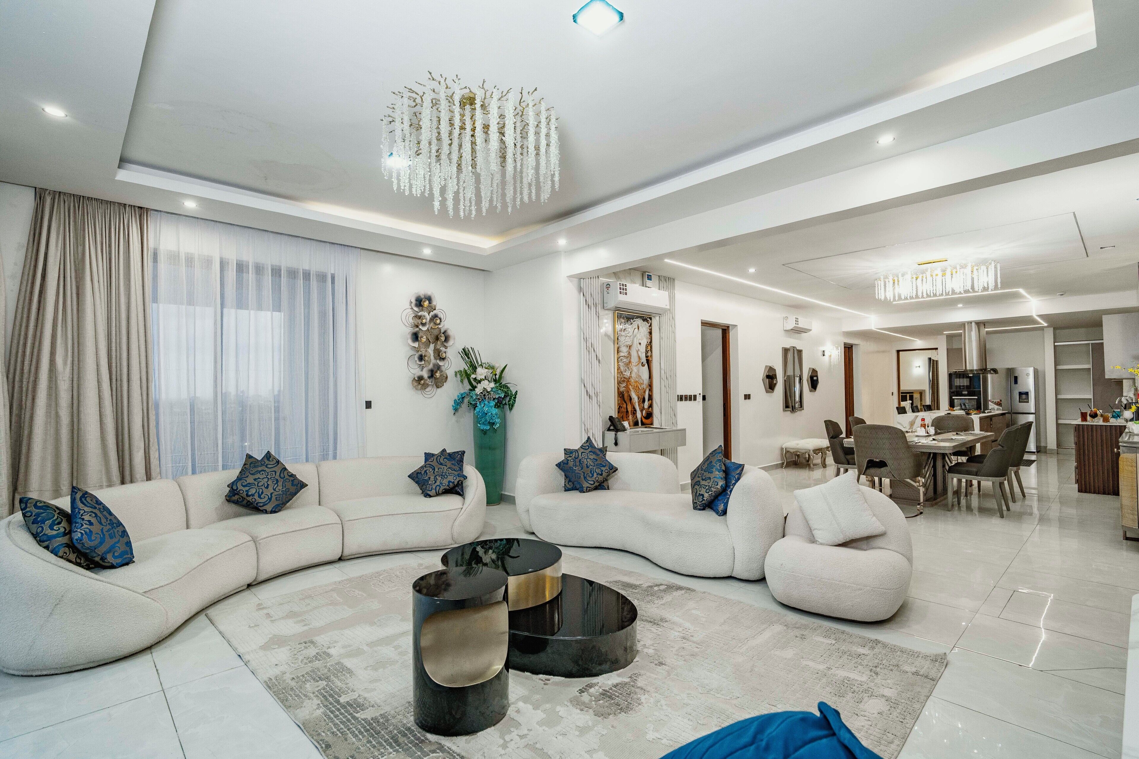 A modern living room with a curved sofa, a coffee table, and a dining area with chairs and a table.
