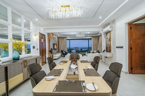 A modern hotel dining area with a long table set for a meal, comfortable seating, and a view of the cityscape. - Mira Heights Suite & Conferencing (Mombasa)