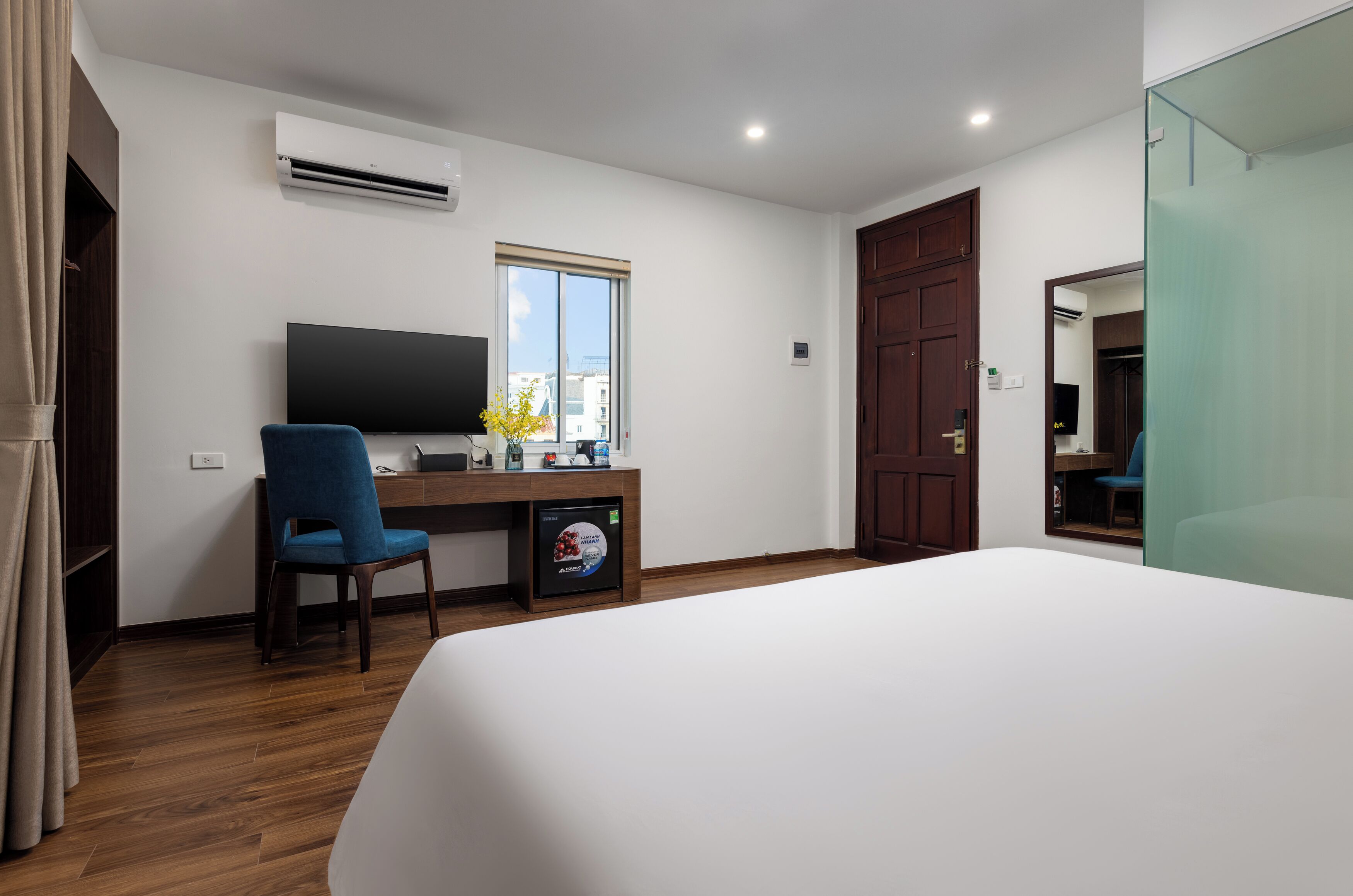 Quarto de hotel com cama, escrivaninha com computador, cadeira, ar condicionado e janela.