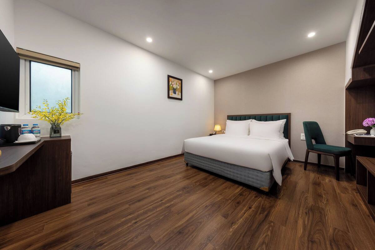 Ein Hotelzimmer mit Bett, Schreibtisch, Stuhl, Fenster mit Aussicht und einem Bild an der Wand.