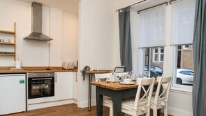 Eine kompakte Küche mit Einbauofen, kleinem Kühlschrank und einer Essecke mit Holztisch und weißen Stühlen.