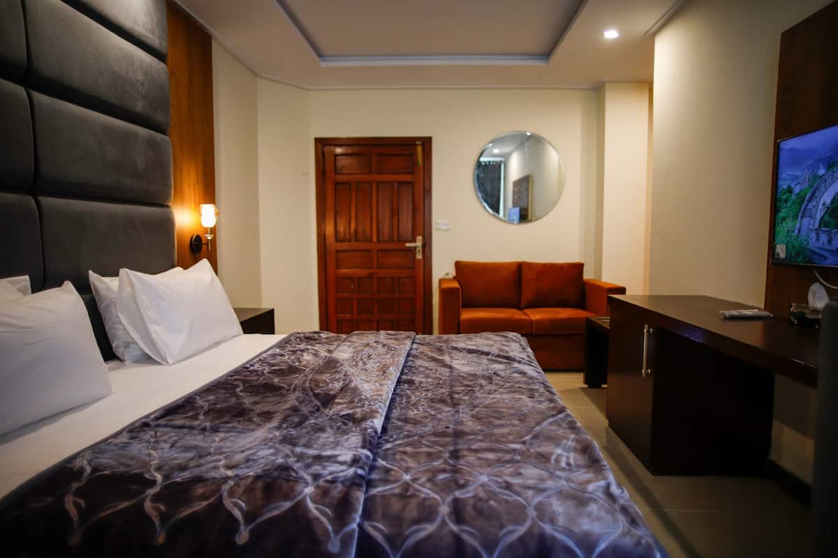 Habitación de hotel con una cama grande, una puerta de madera, un espejo redondo, un sofá naranja, un escritorio y un televisor.