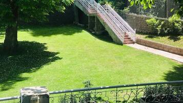 A grassy area with a staircase leading to a higher level, surrounded by a fence and trees.