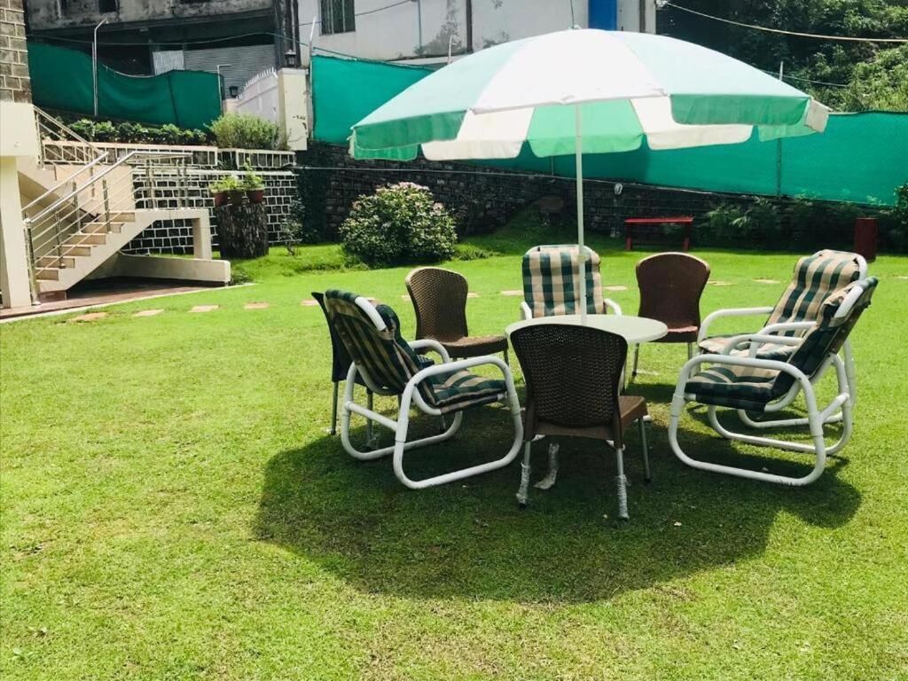 A patio area with a table and four wicker chairs, a green and white umbrella, and a staircase leading to a building.
