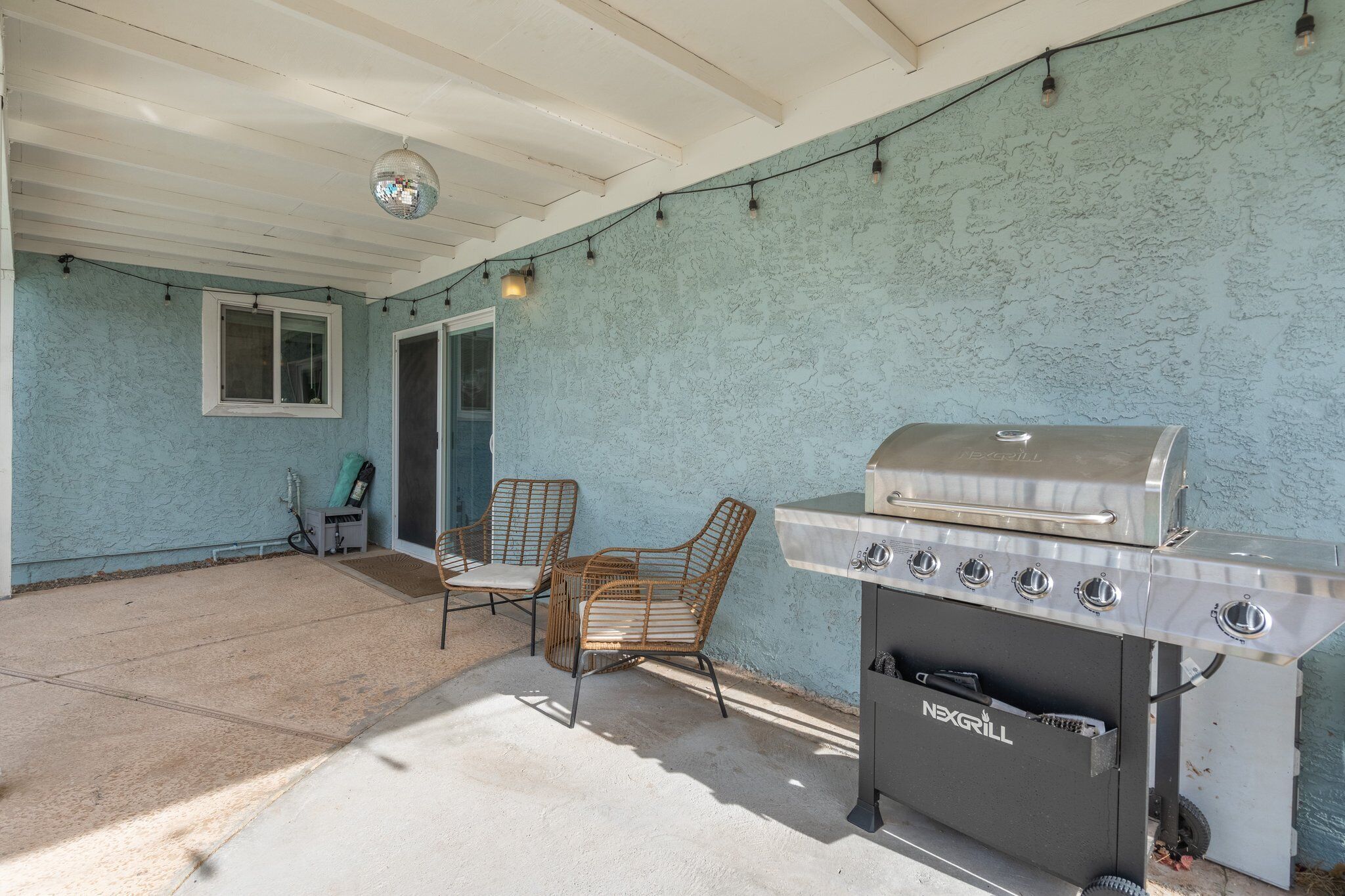 Un patio exterior con una parrilla, sillas y una ventana.