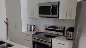 A modern kitchen with white cabinets, stainless steel appliances, and a wooden floor.