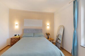 Un dormitorio con cama, mesitas de noche, un espejo y una lámpara de pared.