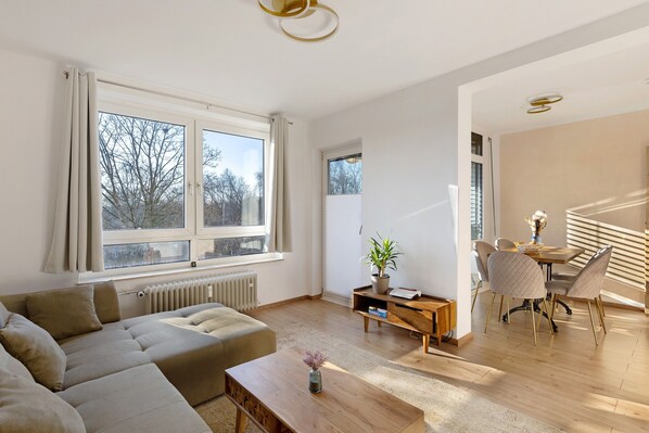 A modern living room with a sofa, coffee table, dining table, chairs, and a potted plant.