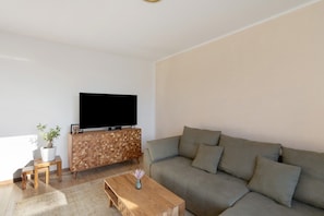 Una sala de estar con un sofá, una mesa de centro, un televisor sobre un mueble de madera y una planta pequeña en una mesita auxiliar.