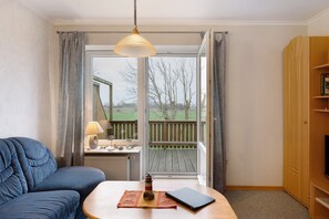 A room with a blue sofa, a wooden table with a lamp, a laptop, and a view of a wooden deck outside. - Apartment 'Annette' with Shared Terrace, Shared Garden and Wi-Fi (Nordstrand)
