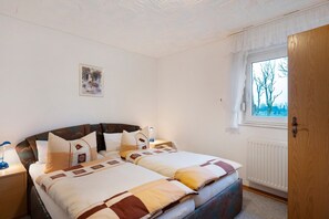 Een slaapkamer met een tweepersoonsbed, een nachtkastje met lamp, een raam met uitzicht op bomen en een radiator.