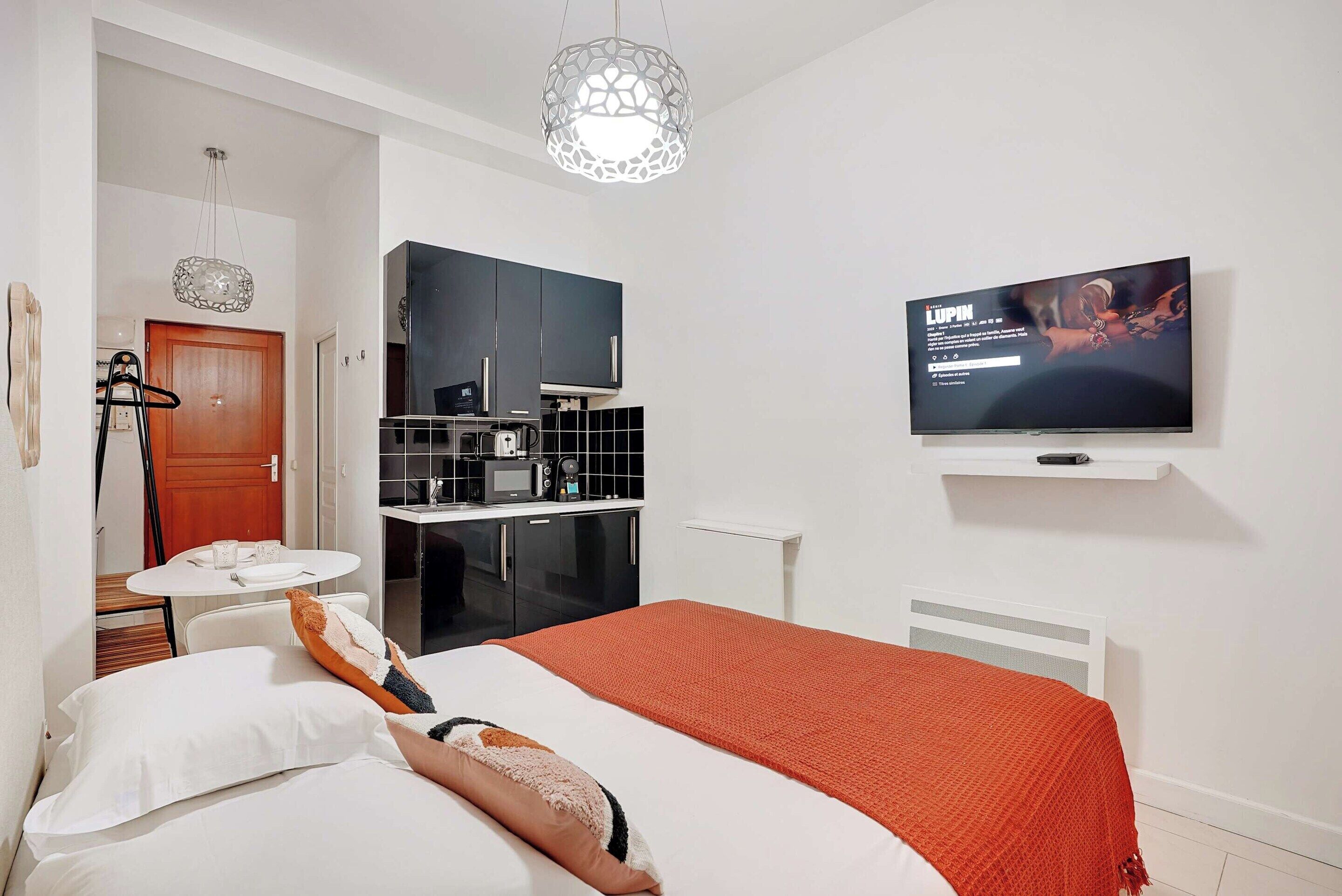 A hotel room with a bed, a TV, a kitchenette, and a dining table.