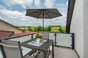 Ein Balkon mit Tisch, Stühlen, Sonnenschirm und Blumen in einer Vase.