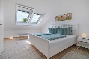Une chambre dotée d’une lucarne, d’un lit avec une literie bleue, d’une table de chevet avec une lampe et d’une œuvre d’art murale.