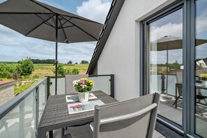 Un balcon avec une table, des chaises, un pot de fleurs et un grand parasol.