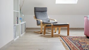 Una habitación moderna con una silla de madera, un pequeño banco, un tapiz estampado y un tragaluz.